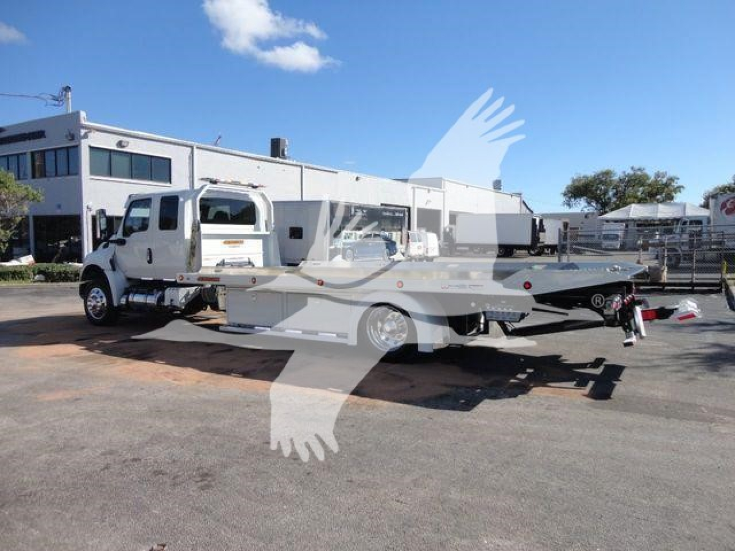 Truck with a rollback bed showing a white cab and long flatbed in a dealership lot.