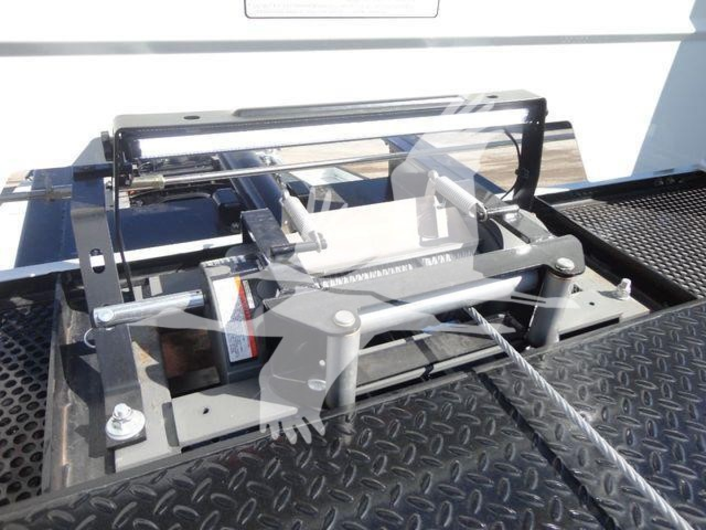 Truck bed equipment showing a hydraulic rollover mechanism with metal frame and levers, mounted on diamond-plate surface.
