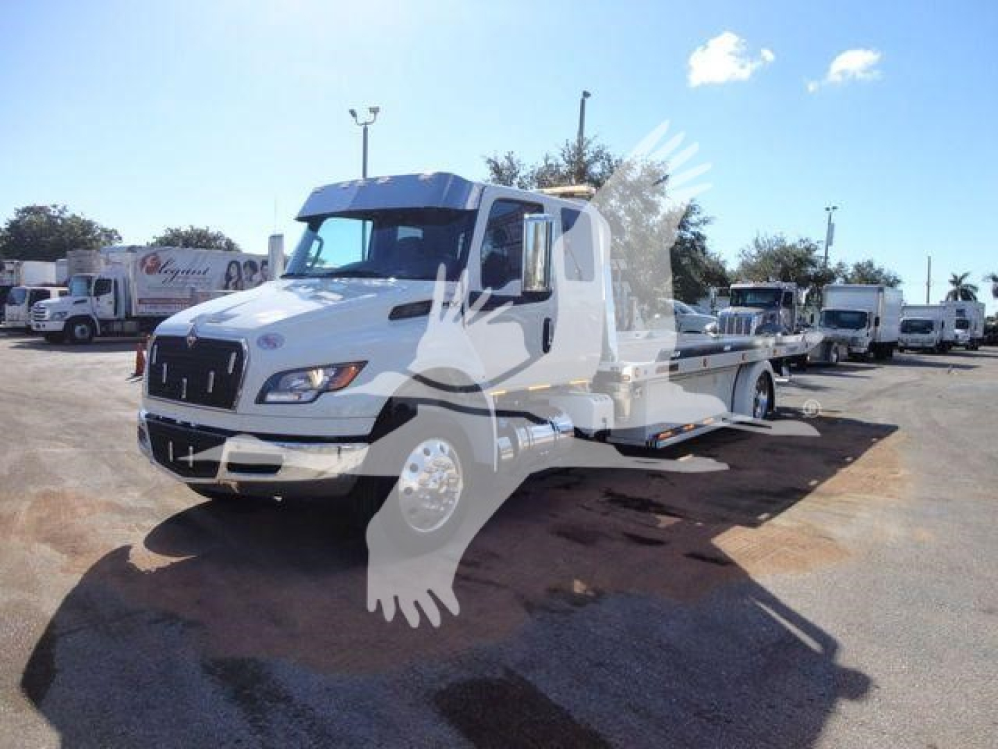 International MV tow truck (rollback) in a vehicle lot, front-left view showing the cab and flatbed carrier.