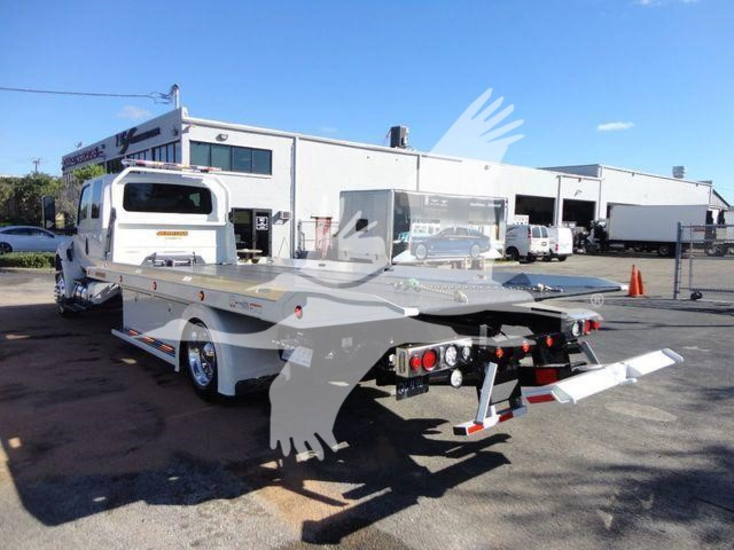 Tow truck with a flatbed load bed and crane hook, rear view showing dual axle and rear lighting; International MV rollback truck.
