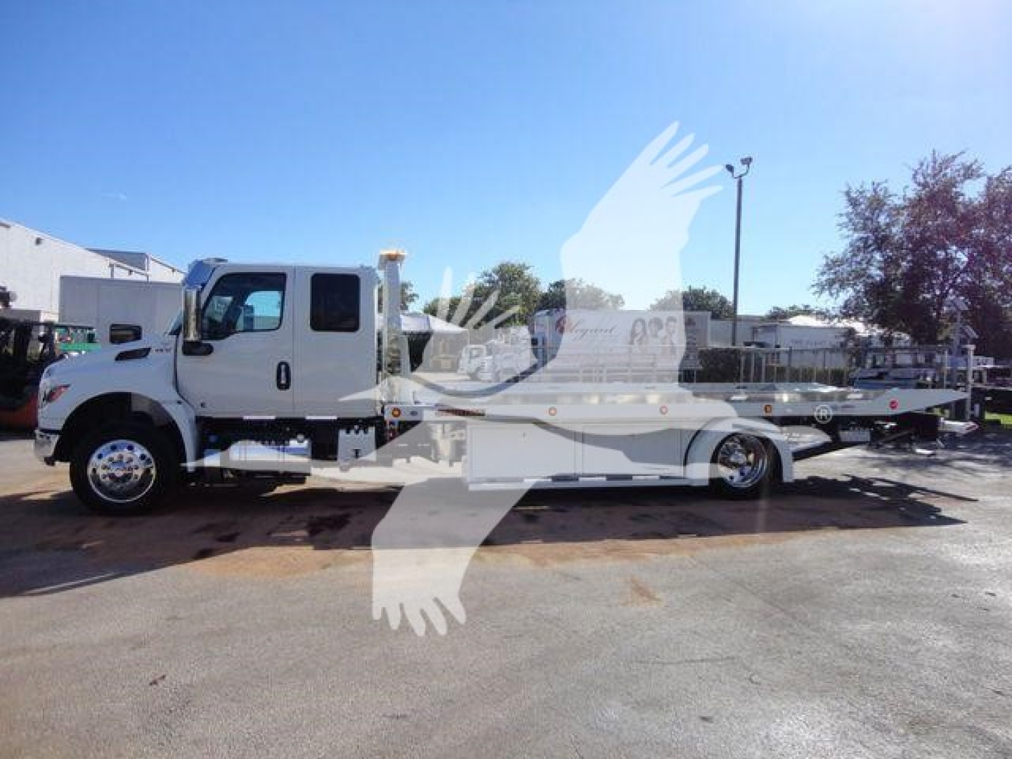 International MV rollback truck in-service with a white cab and a long flatbed, side profile visible.