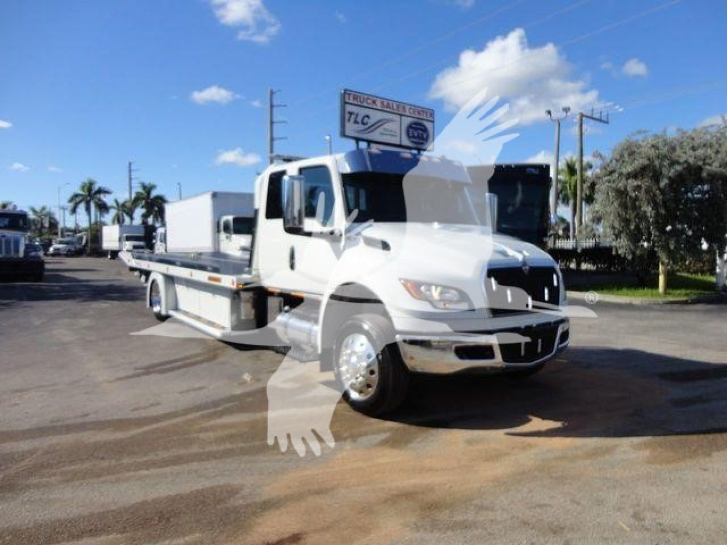 Truck in a dealership lot displaying a white International MV cab with flatbed and a sign above.