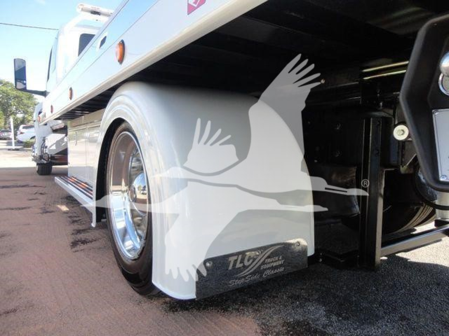 Truck side undercarriage view showing wheel, mudflap, and TLC badge on fender with chrome rims.
