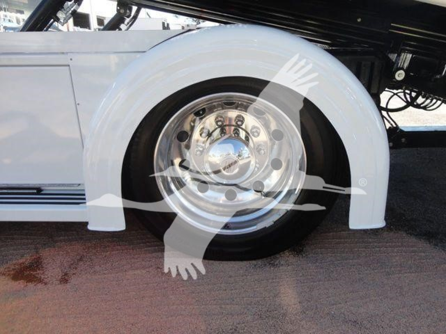 Truck wheel and fender showing polished aluminum wheel with lug nut pattern and Volvo white mudguard around tire on International MV chassis.