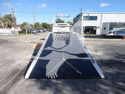 Tow truck ramp viewed from front, flatbed with two hand-drawn safety chains and clear area, International MV in a dealership lot.