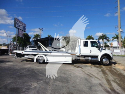 Tow truck with a flatbed in service bay showing a white International MV chassis and long wheelbase flatbed.