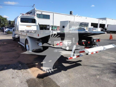 Flatbed tow truck in service bay showing long mechanical bed and rear loading ramps with safety lights and reflective tape.