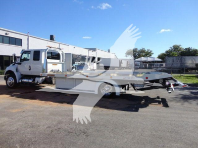 Truck chassis with flatbed tow body attached and a white International MV cab, side view, in a lot.