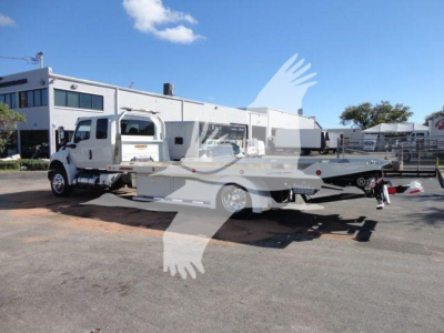 Truck with a rollback bed showing a white cab and long flatbed in a dealership lot.