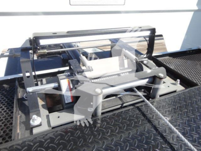 Truck bed equipment showing a hydraulic rollover mechanism with metal frame and levers, mounted on diamond-plate surface.