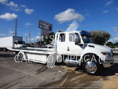 Truck: International MV rollback tow truck with flatbed, white cab, stock number STEPSIDEMV607 visible in background.