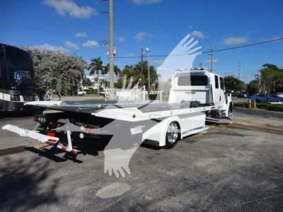 Truck bed tow/rollback equipment attached to a white International MV cab chassis, stock STEPSIDEMV607, new vehicle in a dealership lot.