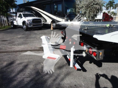 Truck with flatbed or rollback equipment showing towing apparatus and rear hook, with a large black and white motorhome in background.