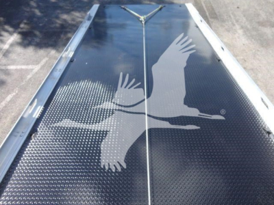 Truck trailer loading area with a large image of two soaring birds in silver on a dark surface, with metal rails along the sides and a center seam.