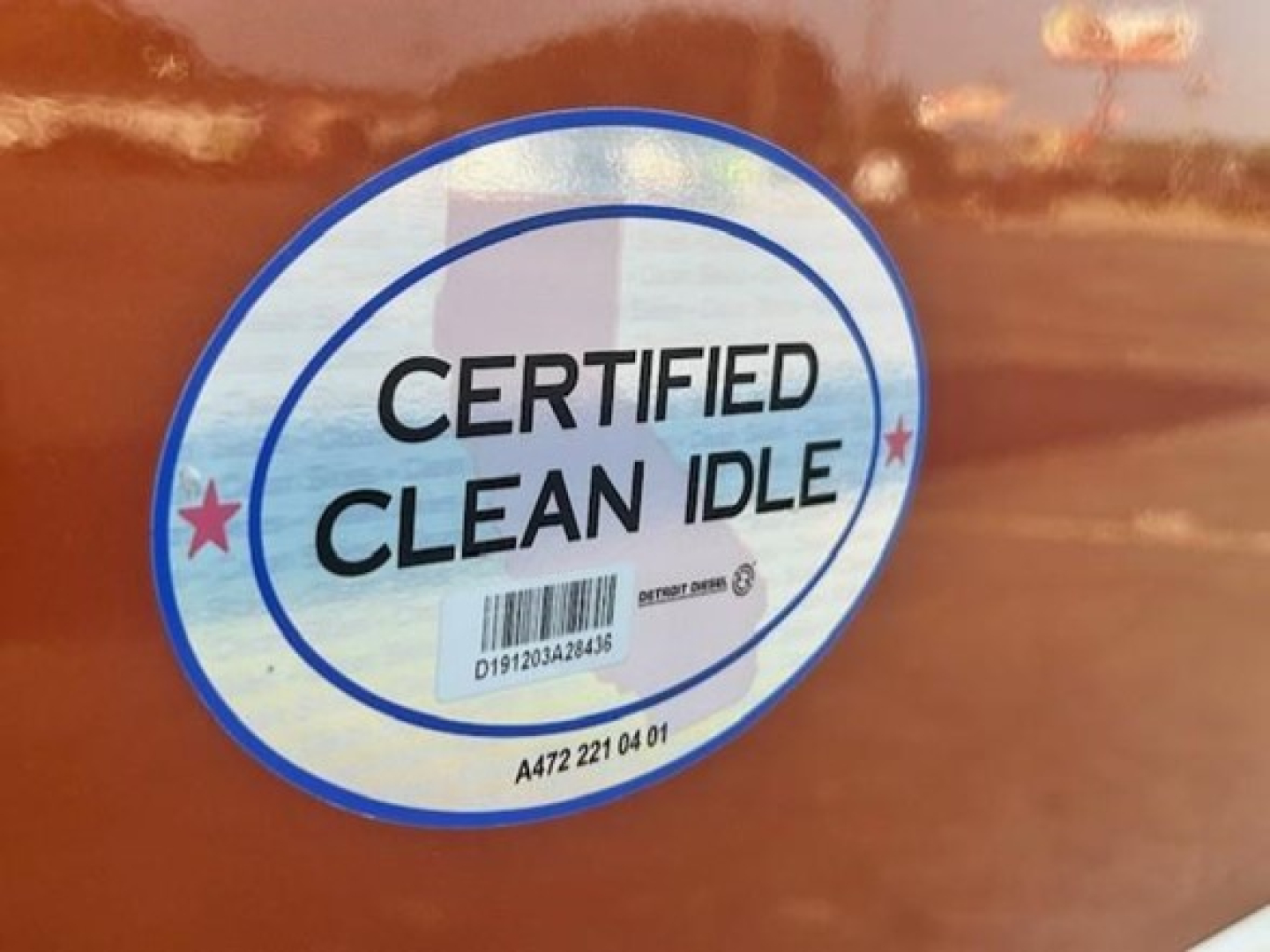 Circular sticker reading CERTIFIED CLEAN IDLE on orange truck body.