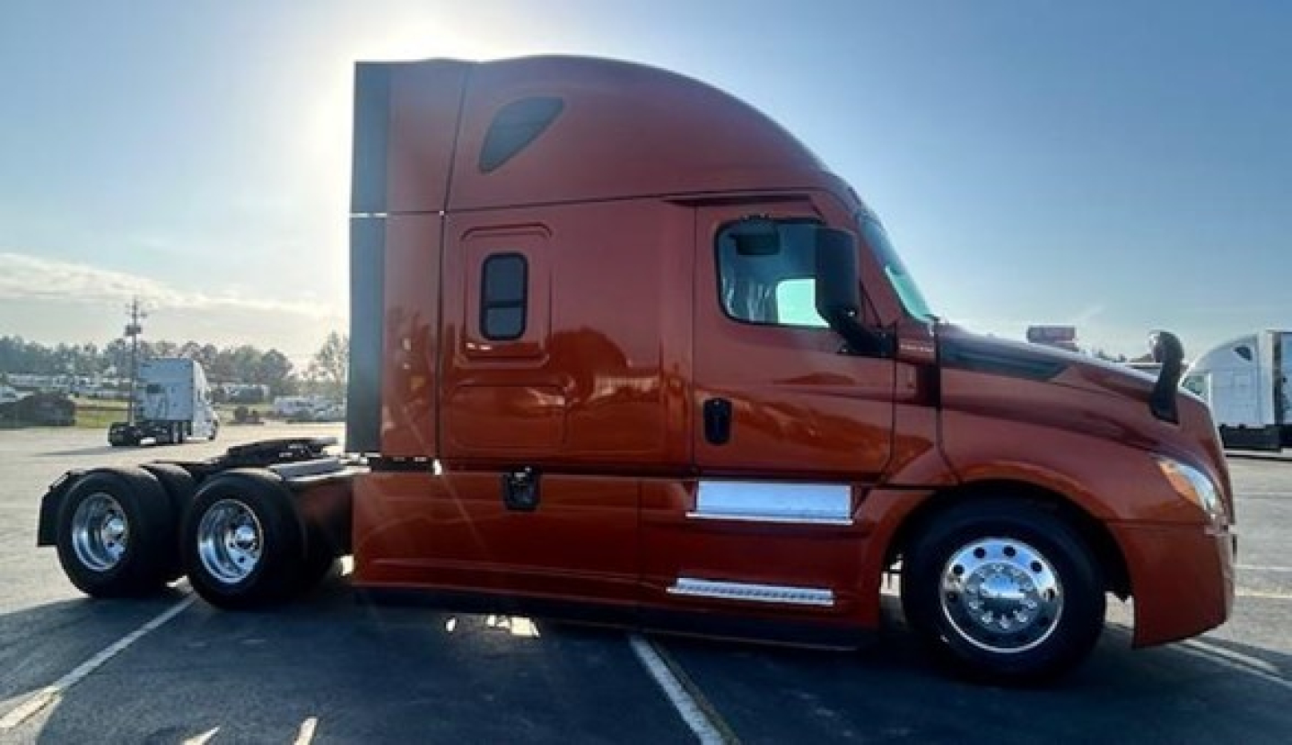 Side view of a 2021 Freightliner Cascadia 126 sleeper cab tractor in brown/orange with chrome wheels and three rear axles visible.