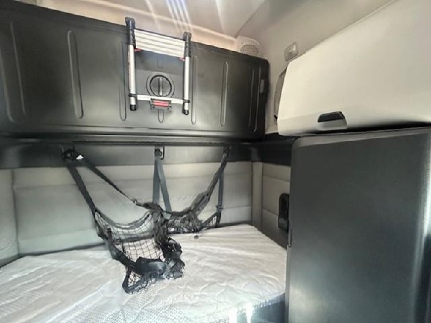 Interior sleeper cab bunk area of a Freightliner Cascadia 126 showing upper bunk storage with strap nets and a mattress.