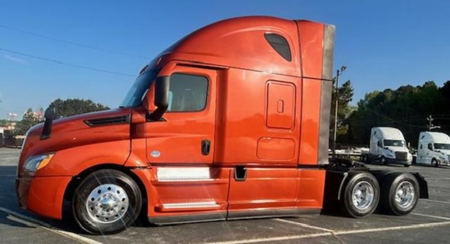 Freightliner Cascadia 126 sleeper tractor side view showing orange cab and dual rear axles.
