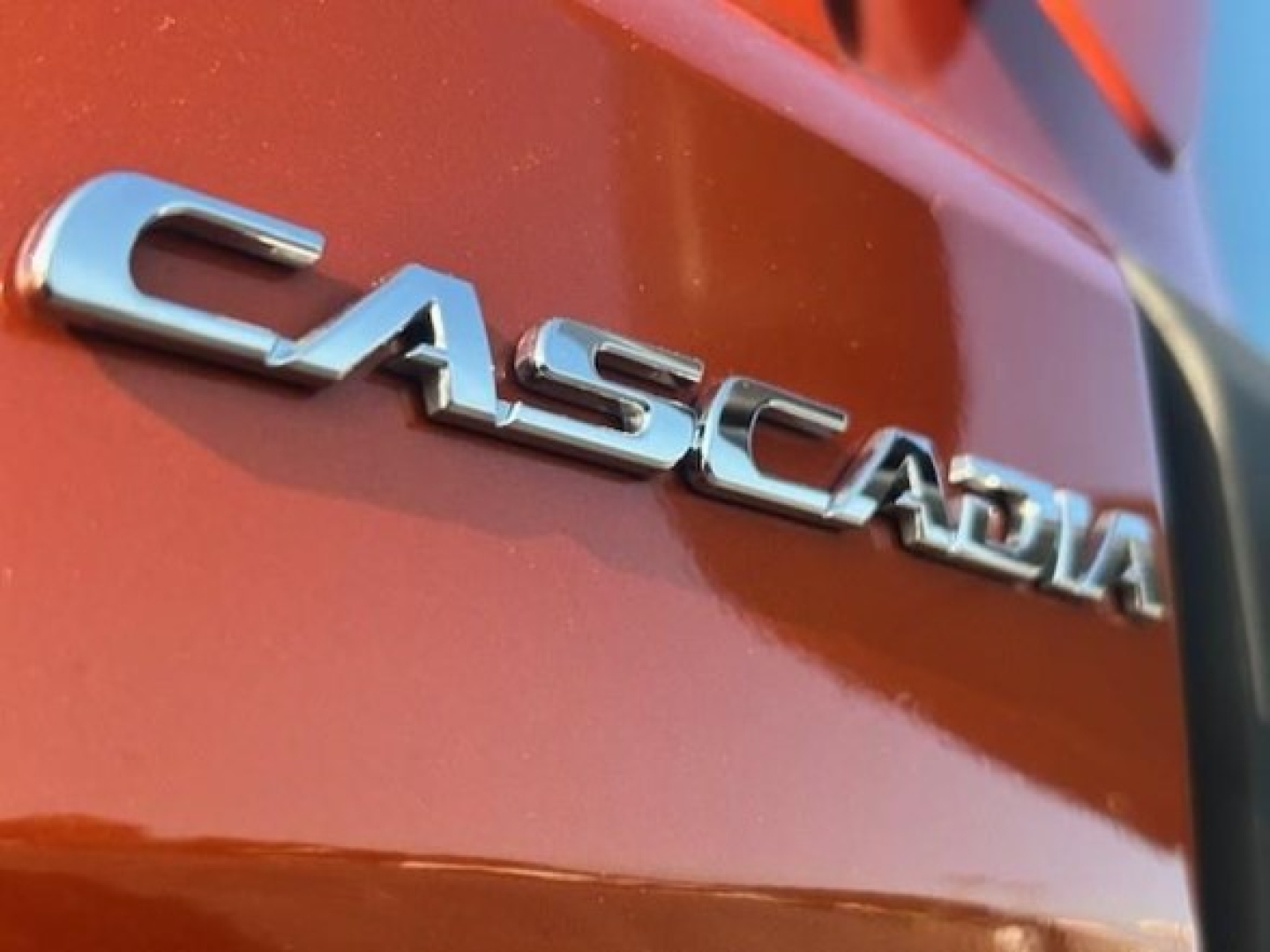 Freightliner Cascadia badge on metallic orange truck rear quarter panel showing CASCADIA text.