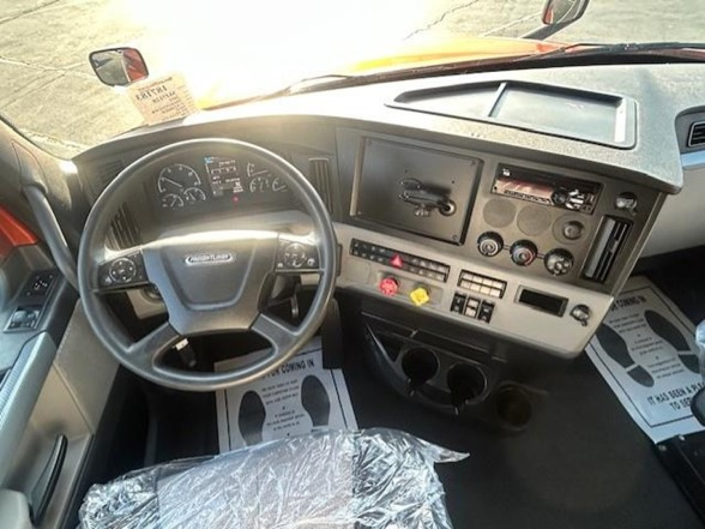Truck cab interior showing steering wheel, dashboard controls, and driver seat area in a Freightliner Cascadia.