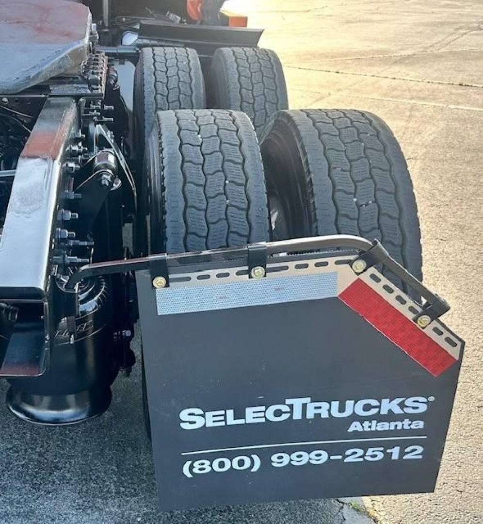 Wheelset and fender area of a Freightliner Cascadia truck showing dual rear axles and a SelectTrucks Atlanta mud flap with phone number.