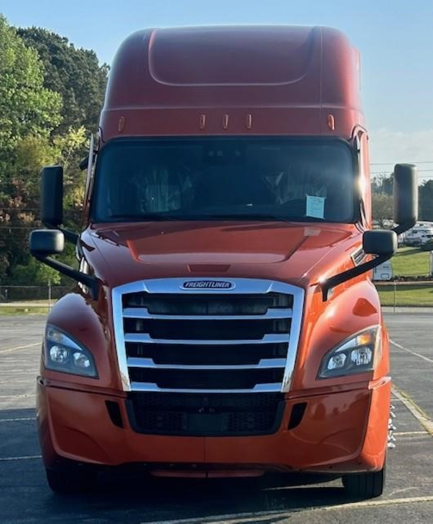 Freightliner Cascadia hood and grille with large chrome horizontal slats, orange paint, headlights, and side mirrors visible.