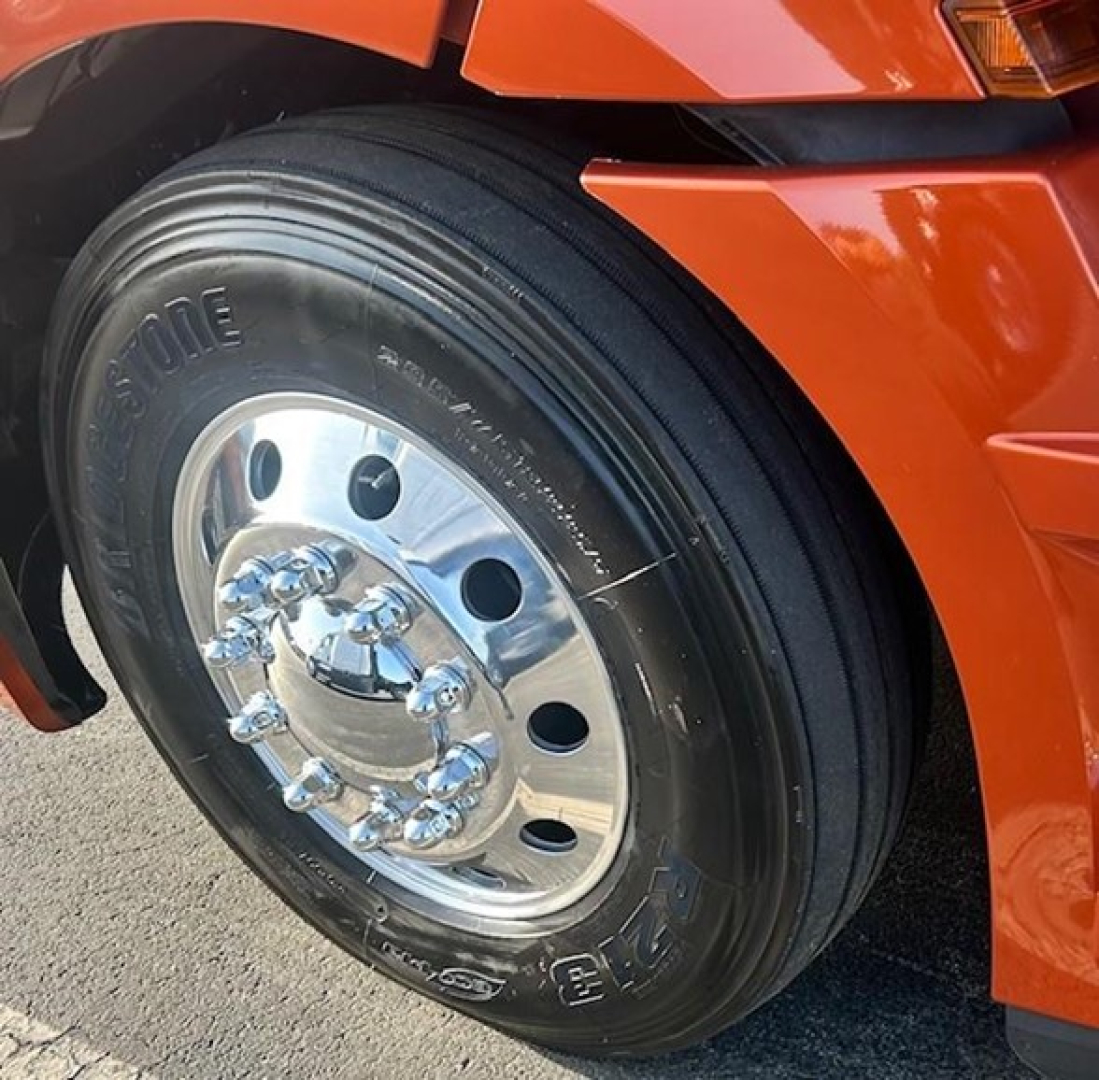 Freightliner Cascadia front wheel showing chrome hub and Bridgestone tire with black sidewall and orange fender.