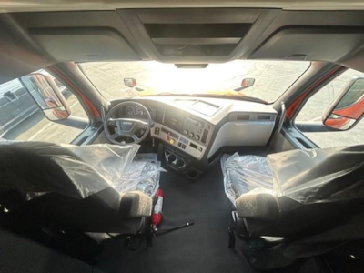Cab interior of a Freightliner Cascadia 126 from driver perspective, with plastic-covered seats, dashboard controls, steering wheel, and center console visible.