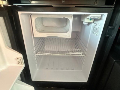 Mini refrigerator/freezer compartment inside Freightliner Cascadia cab with open door and wire shelf.