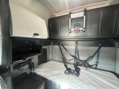 Tractor-trailer cab bunk area with netted storage and overhead compartments in a Freightliner Cascadia sleeper.
