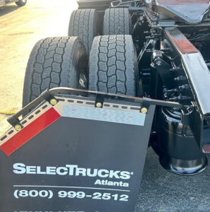 Image shows rear of a Freightliner Cascadia 126 tractor chassis with dual rear axles and mud flaps reading ‘SELECTTRUCKS Atlanta’ and contact number.