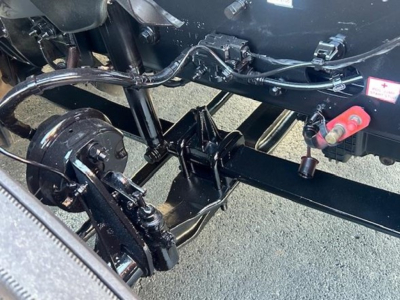 Truck chassis undercarriage showing suspension and drivetrain components with black painted frame and hydraulic lines.