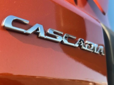 Freightliner Cascadia badge on metallic orange truck rear quarter panel showing CASCADIA text.