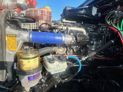 Freightliner Cascadia engine bay showing blue hose, coolant reservoir, and hydraulic reservoir with yellow cap.