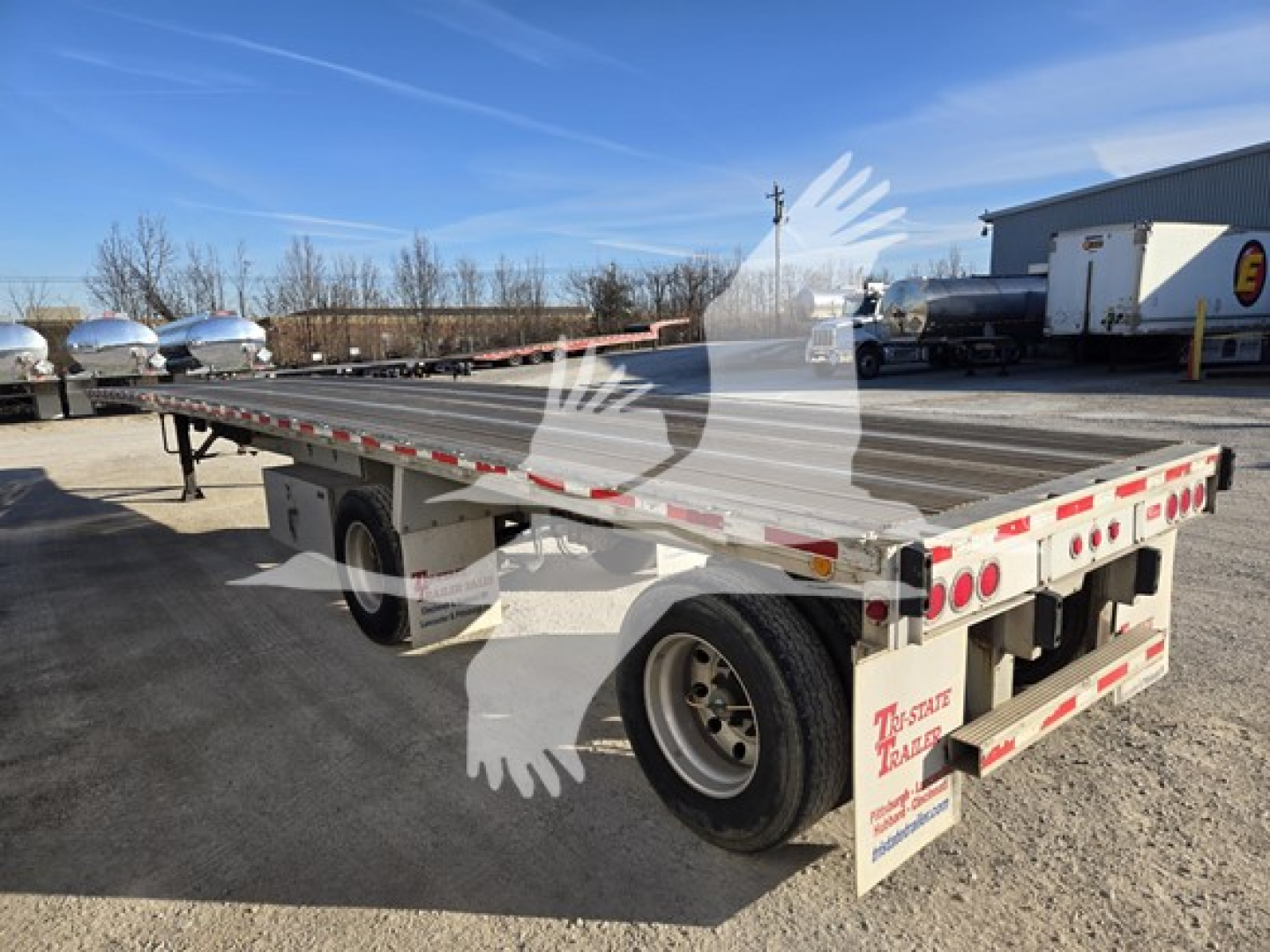 Flatbed trailer showing aftermarket dual rear axles and rear lights with reflective tape and mud flaps.