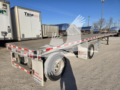 Flatbed trailer showing Maxmiser equipment with reflective safety rails and dual rear lights, long platform, spare wheel, and truck yard background.