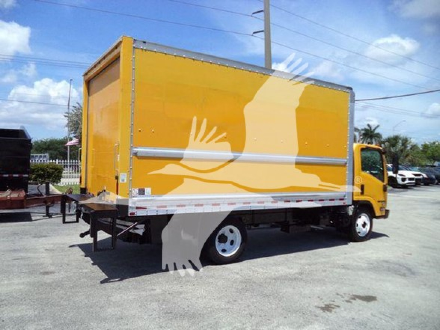Isuzu NPR HD box truck in yellow with cargo box, side view showing rear lift gate and dual rear wheels.
