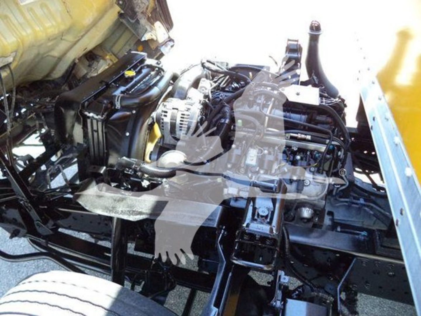 Isuzu NPR-HD truck engine bay exposed showing engine components and wiring with yellow vehicle body nearby.
