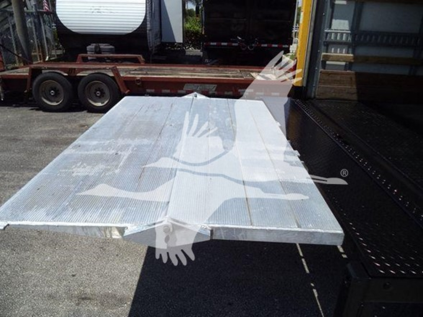 Flatbed aluminum truck bed panels laid on a loading platform with a trailer and warehouse in the background.