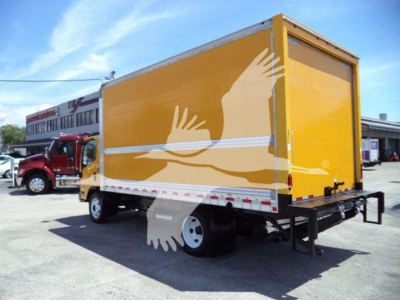 Isuzu NPR HD box truck rear-side view showing yellow cargo box and rear bumper with hitch