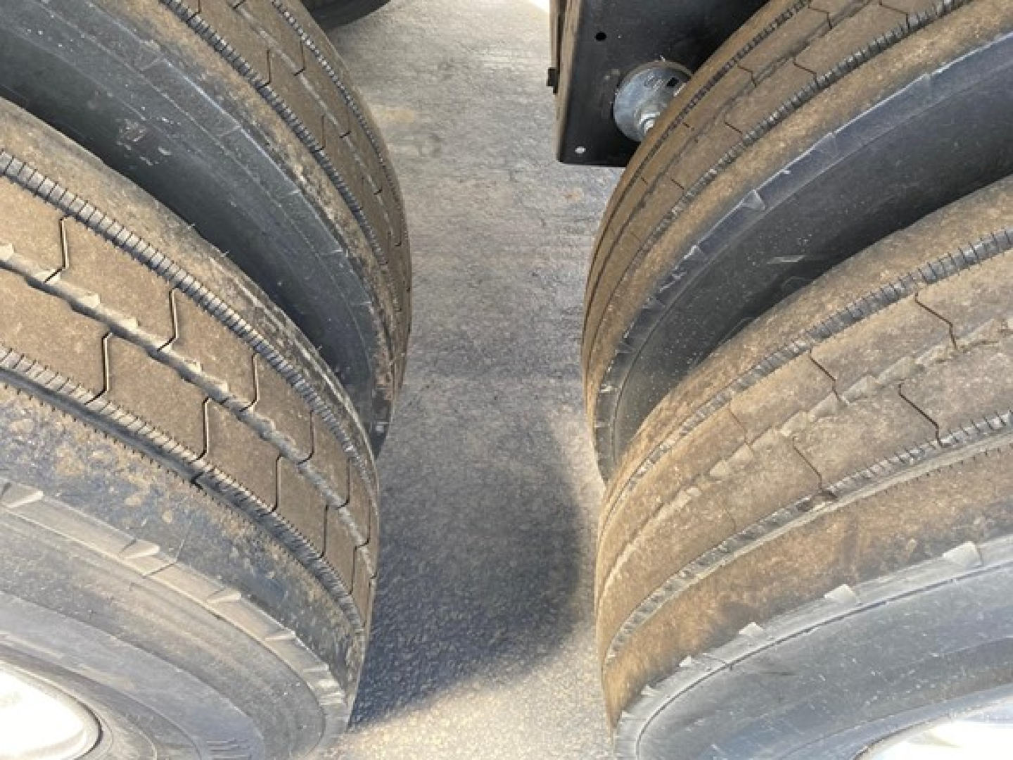 Trailer tires in pairs with tread visible, part of a new Mac Wes dump trailer; focus on dual axle wheels with low tread depth and dirt on road surface.
