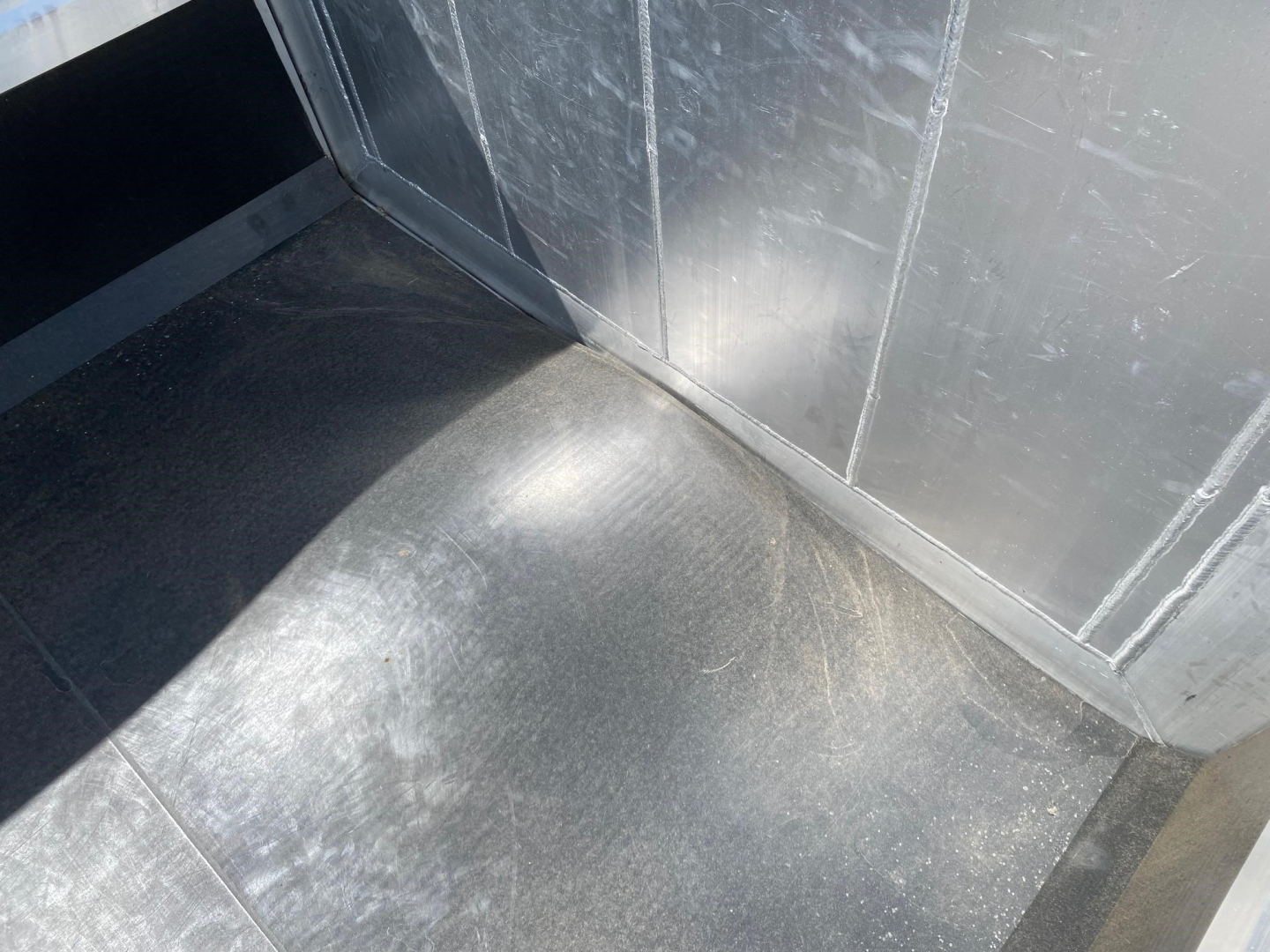 Dock of a new dump trailer interior corner with metal walls and a curved floor surface showing light scuff marks.