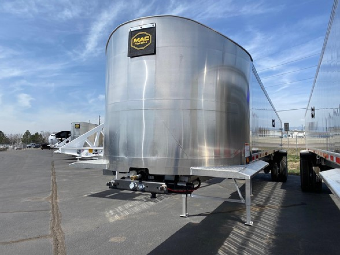 Trailer showing a shiny aluminum dump trailer with Mac trailer logo, front view, dual axle, landing gear, and hitch.