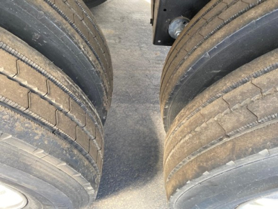 Trailer tires in pairs with tread visible, part of a new Mac Wes dump trailer; focus on dual axle wheels with low tread depth and dirt on road surface.