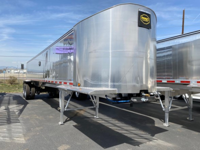 Mac Wes trailer in a lot, polished aluminum dump trailer with blue hitch hoses and Mac logo on front corner.