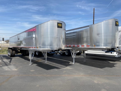 Two silver aluminum dump trailer semitrailers with dual axles and landing gear visible in a dealership lot.