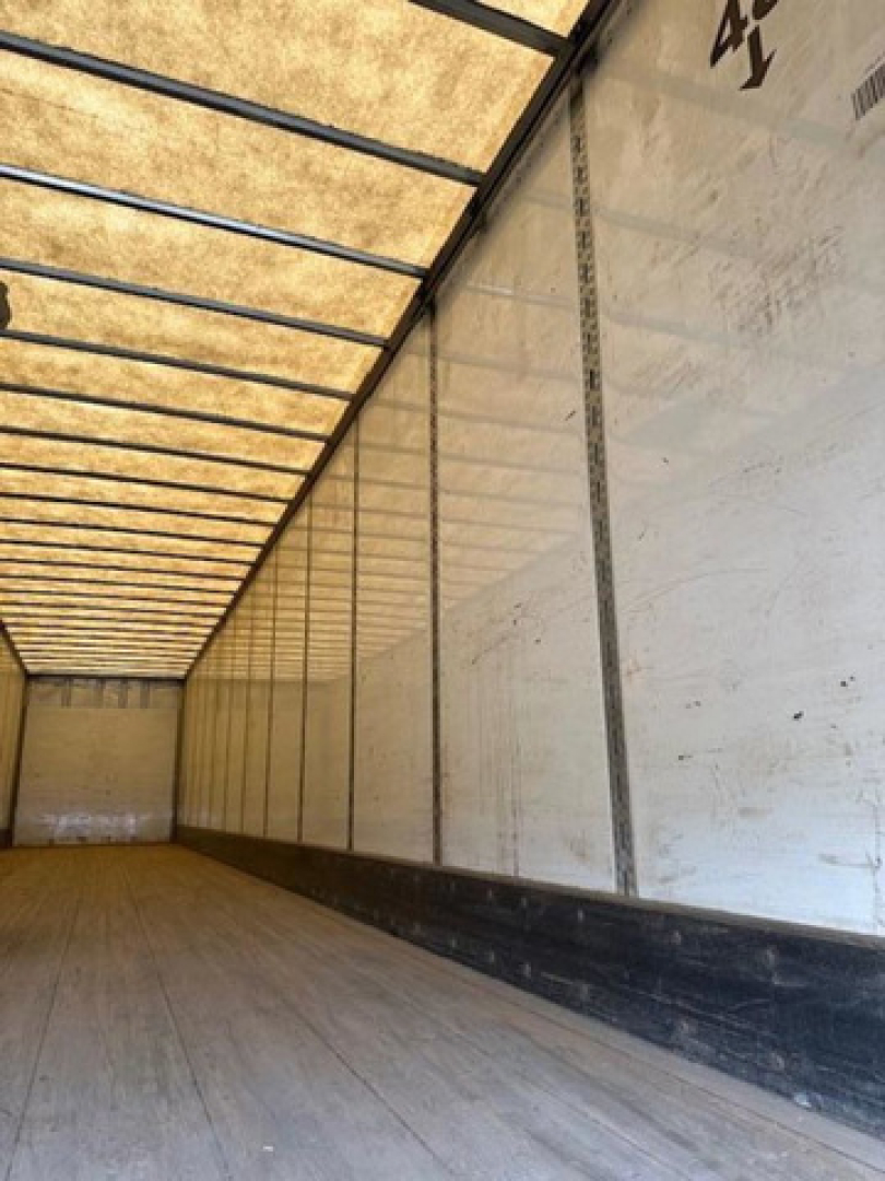 Trailer interior showing empty cargo area with wooden floor and white sidewalls, from rear toward cab area.