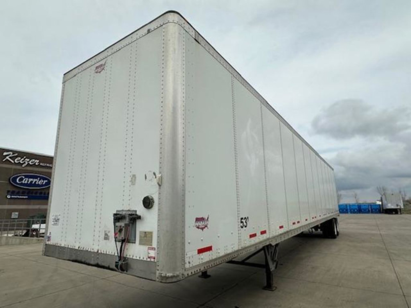 Trailer side view showing a white 53' box with Keijo/Carrier sign in background, rear access door and undercarriage legs.