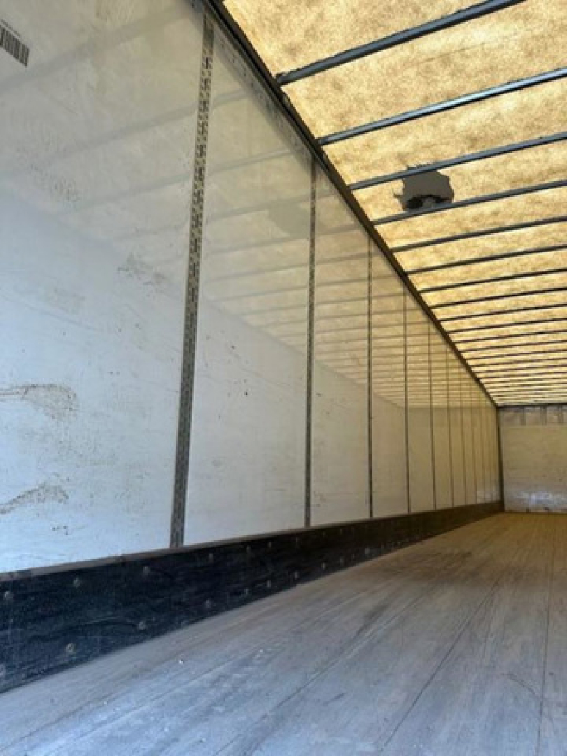 Van trailer interior showing white side walls with vertical supports, wooden floor, and overhead lighting fixture.