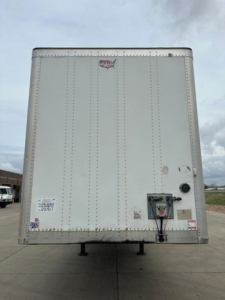 Rear view of a white 2016 Wabash van trailer showing back doors with latches, electrical connection and safety decals.